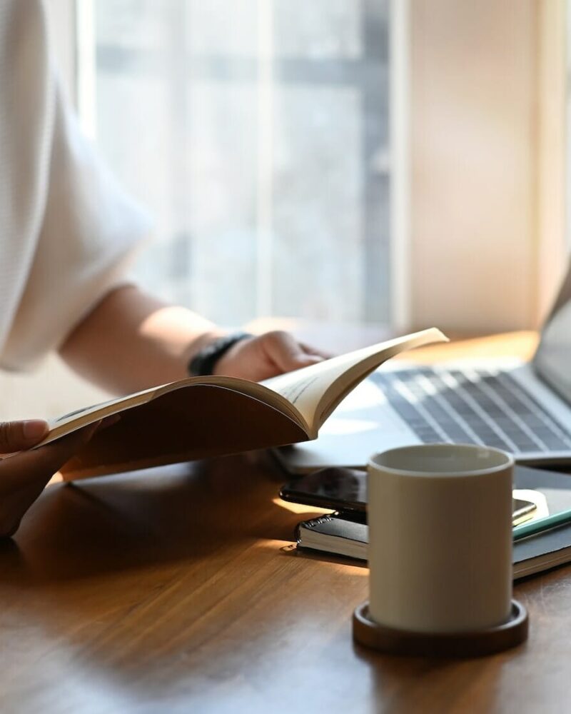 Cropped shot of young designer woman reading a book while sitting at the modern working desk.